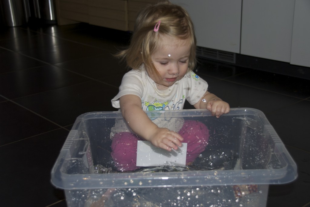 Young child dropping items into a transparent box of water