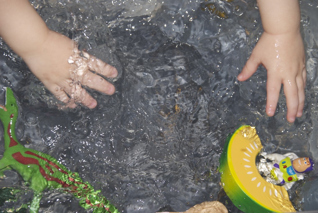 Child's hands in water. Different objects are floating in the the water.