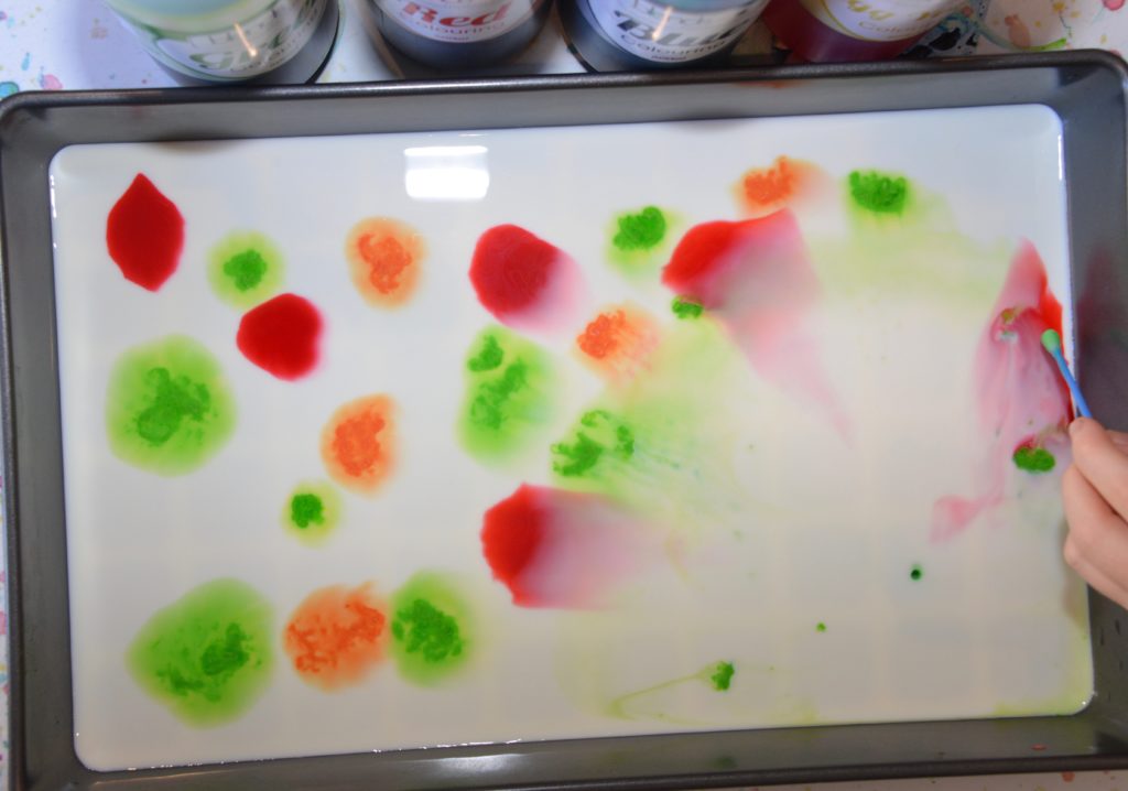 Milk and food colouring in a shallow tray for a magic milk science investigation. The food colouring is spread out over the surface of the milk.