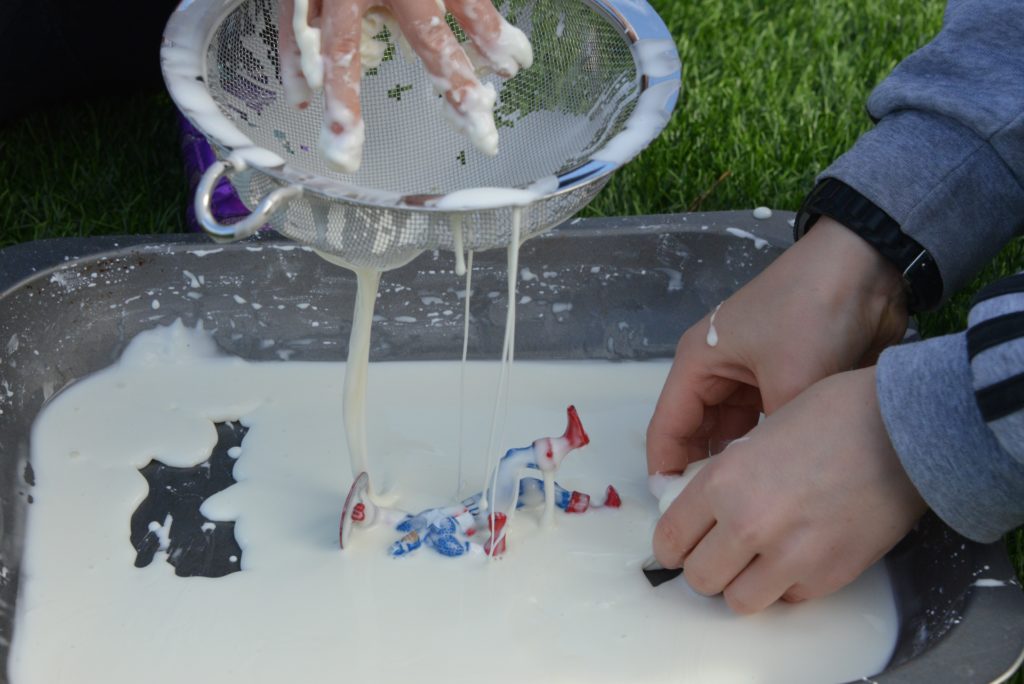 cornflour oobleck in a tray with a sieve and superhero toys