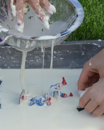 a tray of cornflour and water oobleck with toy figures and a sieve