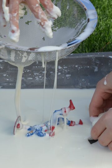 a tray of cornflour and water oobleck with toy figures and a sieve