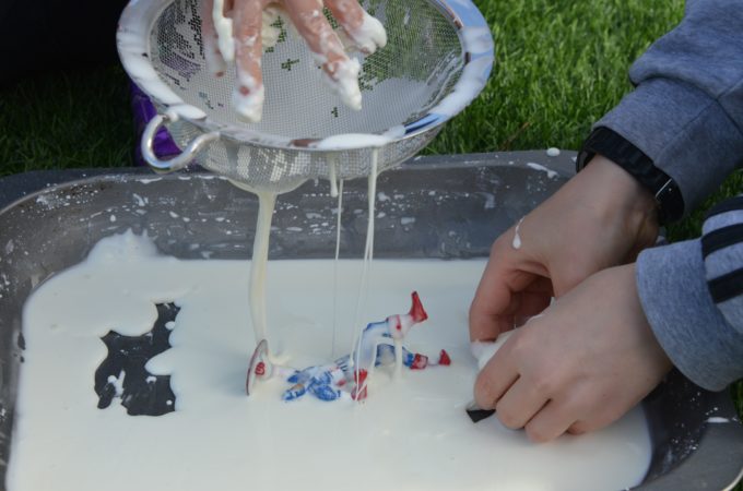 a tray of cornflour and water oobleck with toy figures and a sieve