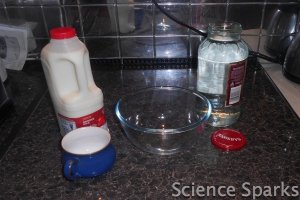 Milk and white vinegar on a counter with a glass bowl.