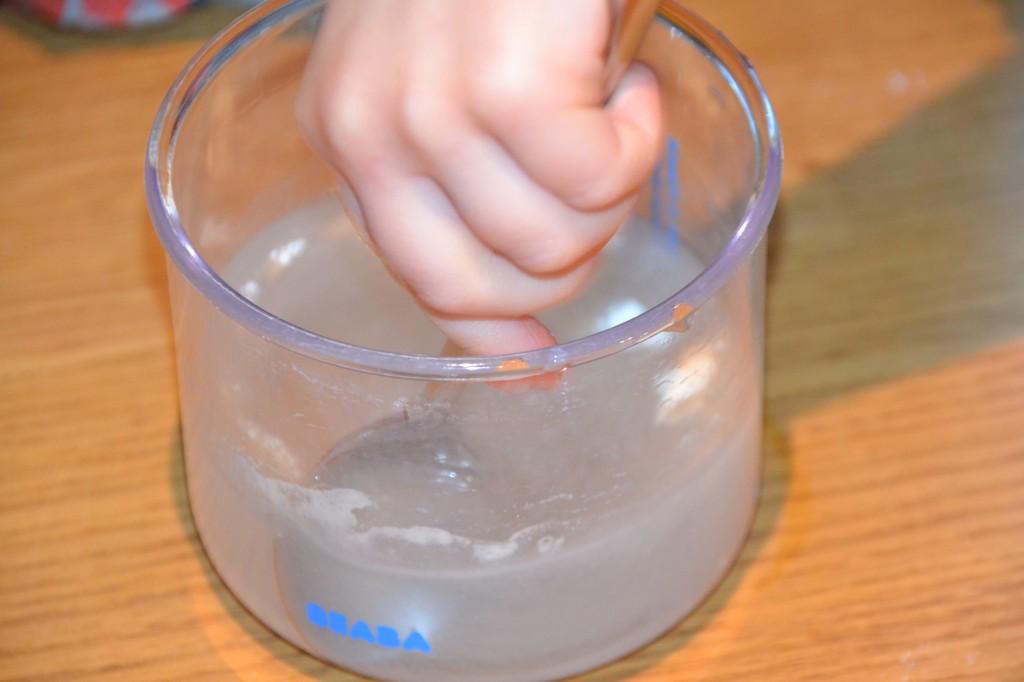 flour and water in a beaker. A child's hand is stirring the mixture to find out if the flour will dissolve in the water.