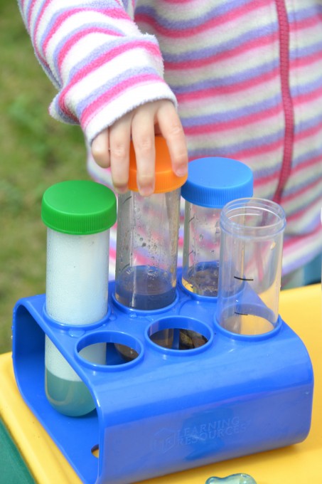 Four test tubes in a rack with different mixtures in. Water and washing up liquid, water and sand and water and mud.