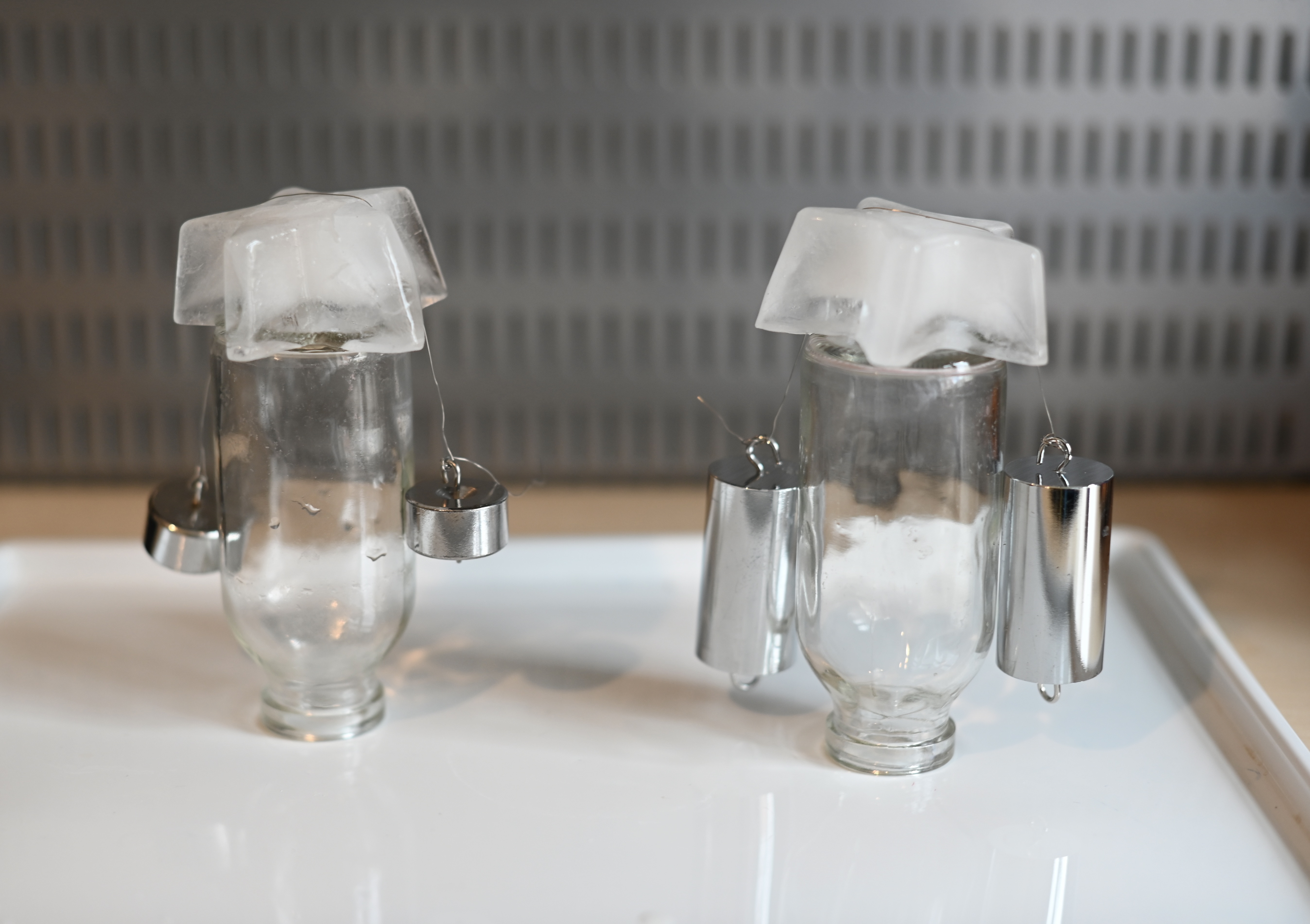 two small containers with an ice cube resting on the top. A thin wire with weights on each end is placed over the ice cube.