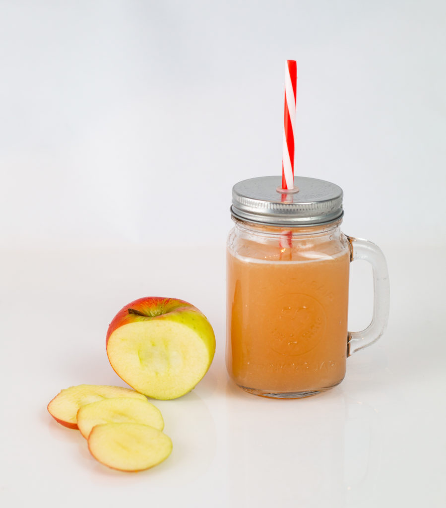 Spiced Apple Cider in a glass drinking cup next to a sliced apple