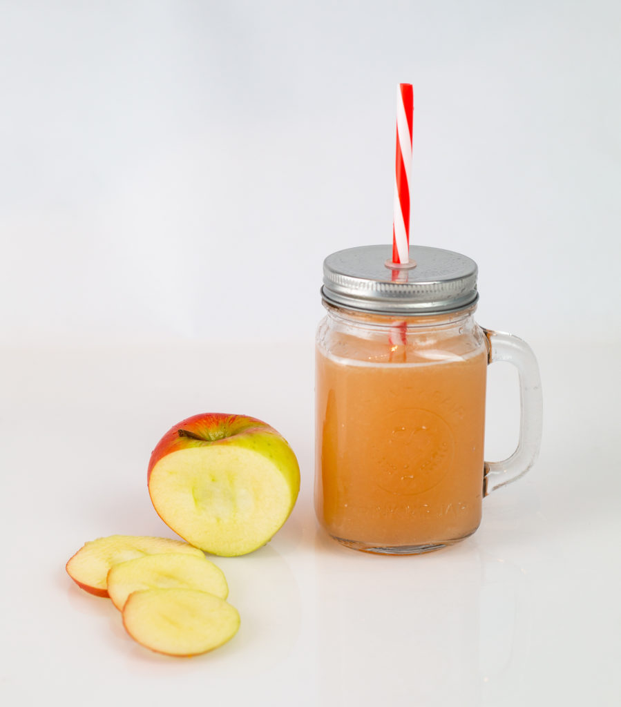 Spiced Apple Cider in a glass drinking cup next to a sliced apple
