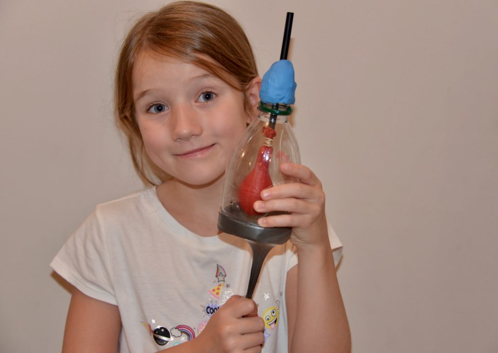 Girl holding a model of a lung made with a plastic bottle, balloon and straw