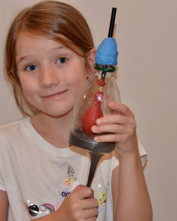 Girl holding a model of a lung made with a plastic bottle, balloon and straw