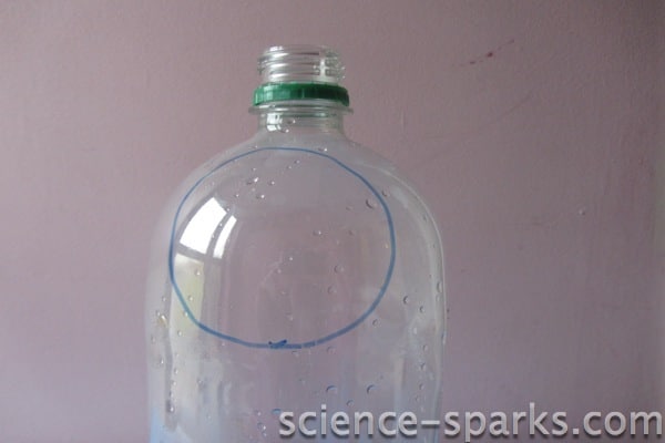 Image of a plastic bottle with a circle drawn on to cut out to make a DIY magnifying glass.
