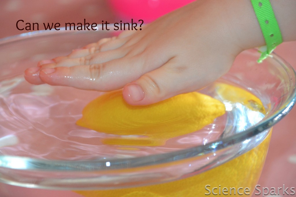 child's hand pushing down on a lemon in a bowl of water