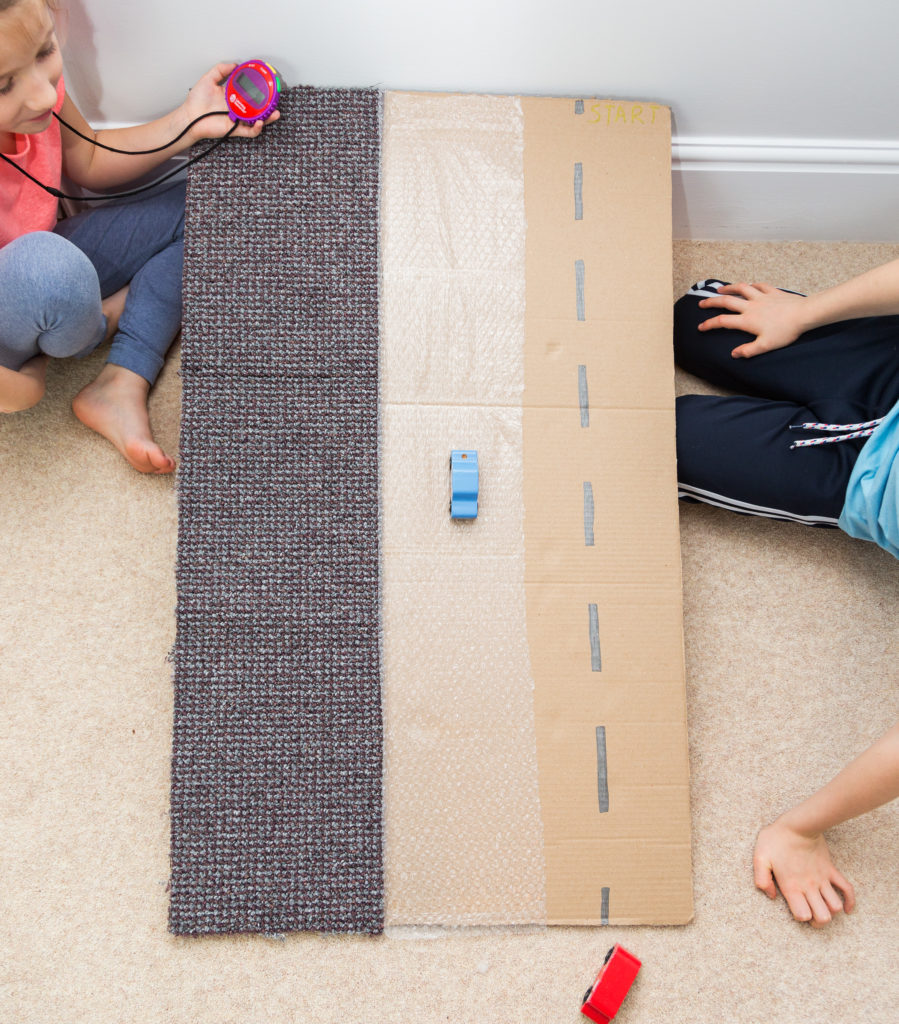 Homemade friction ramp made from a large sheet of cardboard. The ramp has three lanes. One is covered in carpet, one bubble wrap and one just cardboard.