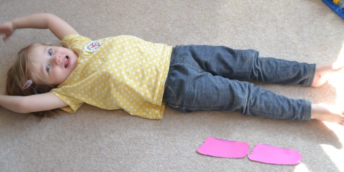 child lying on the floor with cut out shapes of her own feet next to her