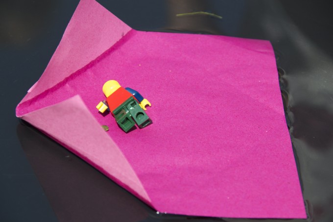 pink paper on water that has unfolded with a LEGO figure floating on top