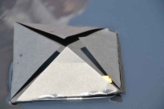 black sugar paper with the four corner folded up on water for a science activity