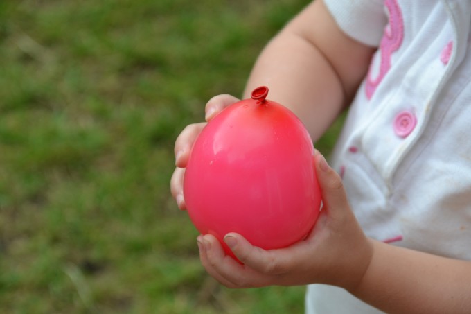 Small child holding a red water balloon