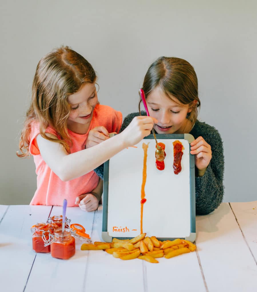 children testing the viscosity of different ketchups by pouring a small sample down a whiteboard ramp