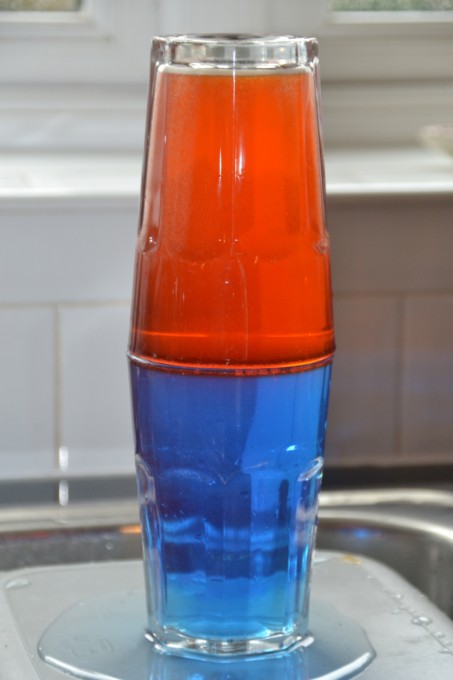 Two glasses on top of each other filled with water, food colouring and different amount of salt. One colour floats on top of the other.