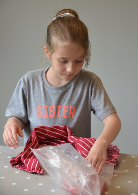 child rolling a bag of ice and salt around another smaller bag filled with smoothie to make a frozen drink.