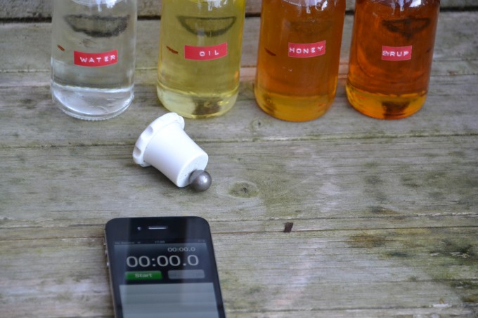 V small jars filled with different liquids for a viscosity experiment