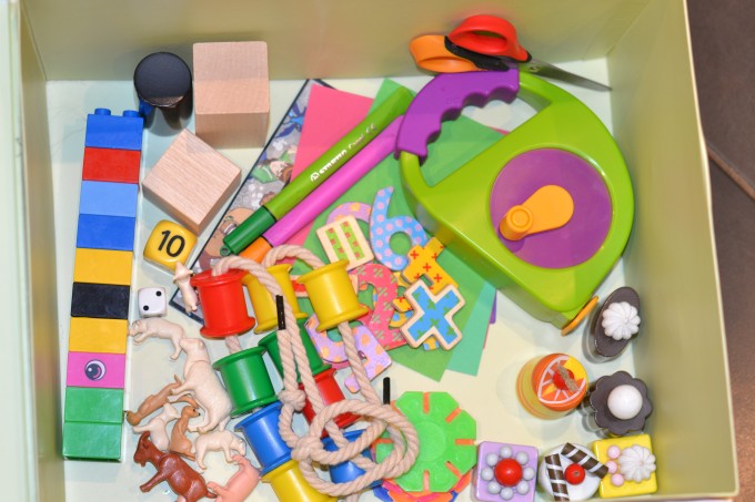 cardboard box filled with duplo blocks, scissors, tape measure, small plastic animals  and other learning items