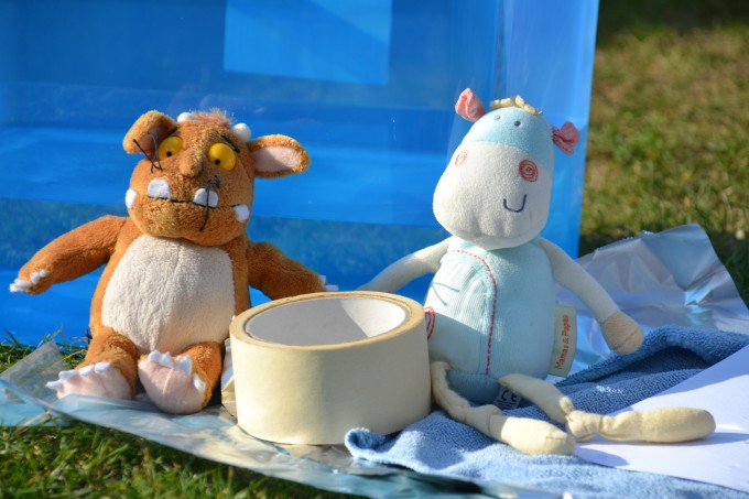 two soft toys outdoors sat next to masking tape, kitchen foil and fabric for a science activity about properties of materials