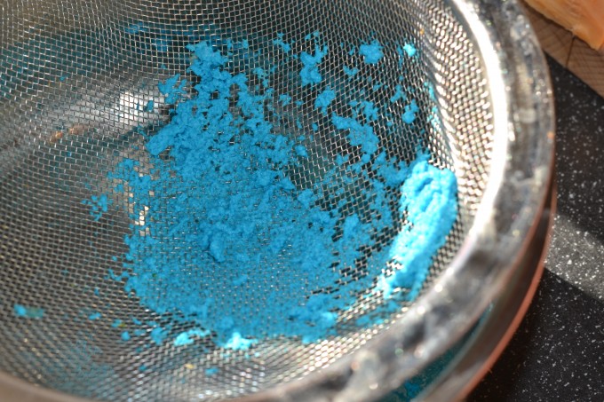 Curds of milk that have been separated from the way using white vinegar and a sieve. The curds are in a sieve and are blue from food colouring.