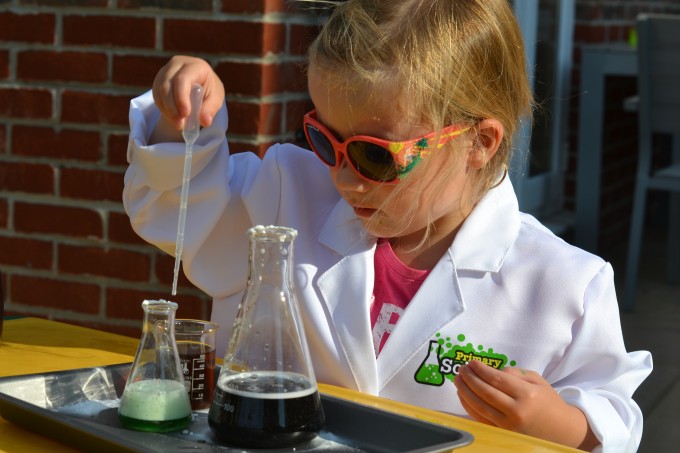 a child sat outside in from of containers filled with coloured liquids and fizzy potions