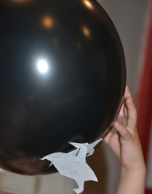 tissue paper shaped ghosts attached to a black balloon by static electricity for a Halloween science experiment.
