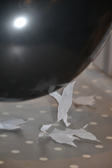 black balloon with a tissue paper ghost shape hanging from it because it has been charged with static electricity