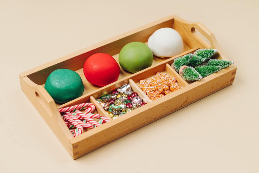 Christmas coloured balls of play dough with small festive decorations in a wooden presentation box.