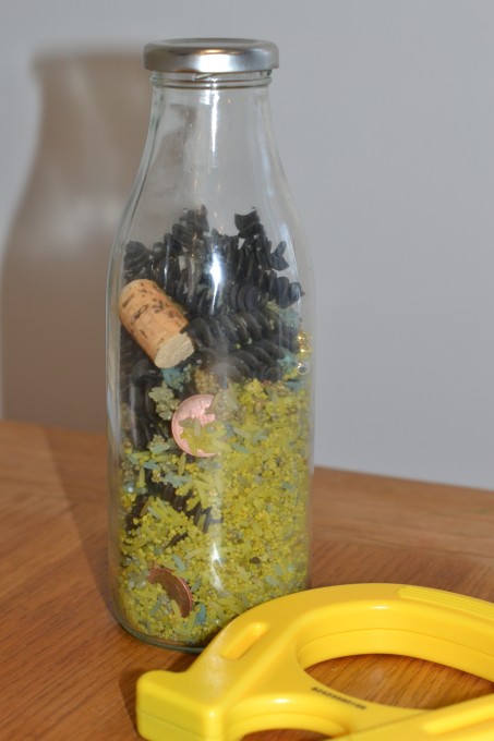 glass bottle containing coloured rice and magnetic and non magnetic objects for a sensory bottle.