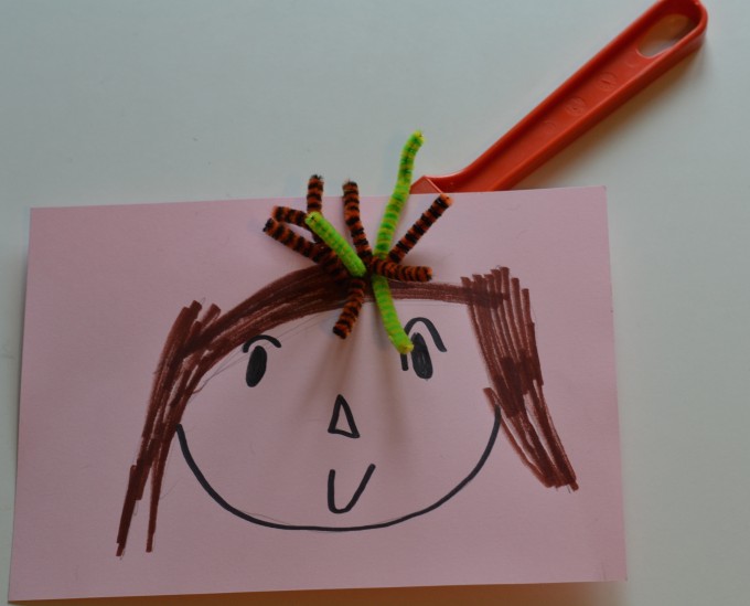 a drawing of a head with hair. On top of the head are segments of pipe cleaner cut to look like hair. Under the paper is a magnet wand