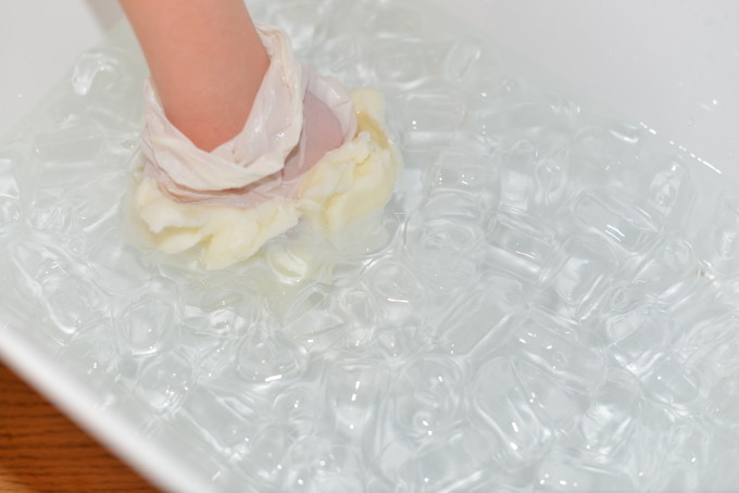 a gloved hand covered in lard in a tray of icy water for an arctic animal science experiment