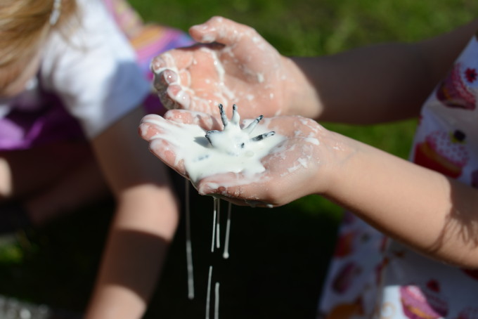 a small plastic toy spider in a child's hands covered in white cornflour gloop