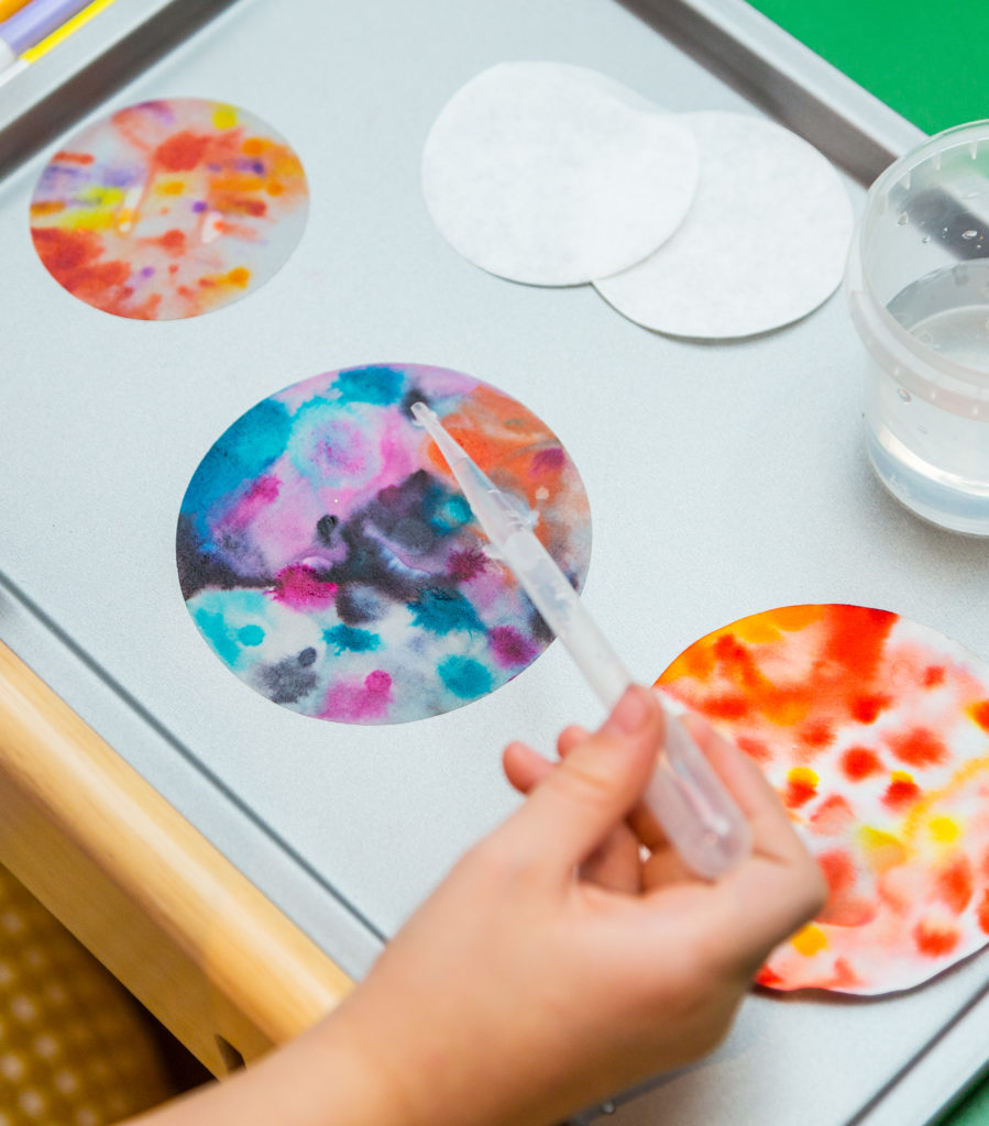 Chromatography craft made to look like planets of the solar system. A child is dripping water from a pipette onto a small circle of filter paper made to look like a planet.