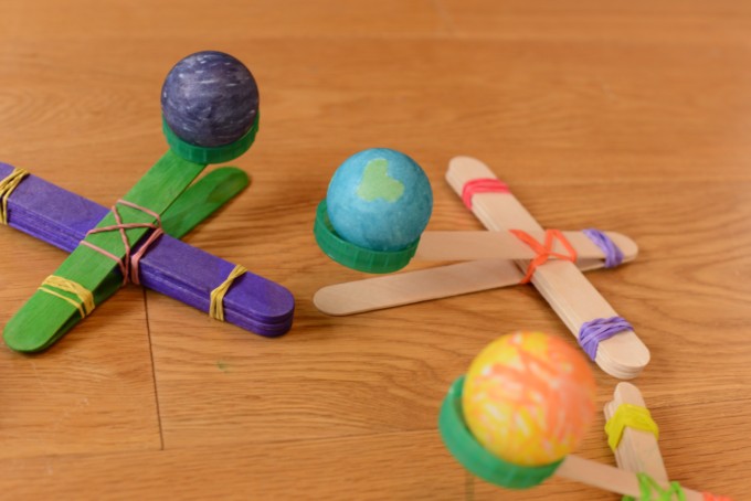 Image of 3 space themed lolly stick catapults made with craft sticks, milk bottle tops and elastic bands