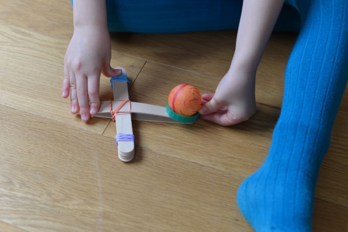 child pushing down on a craft stick catapult
