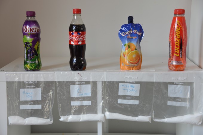 How much sugar is in kid's drinks? Bottles of drink with the amount of sugar weighed out to the side.