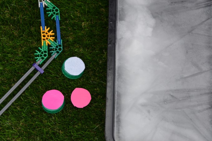 Image of an oven dish filled with ice. Milk top hockey pucks covered in different materials and a K'nex hockey puck
