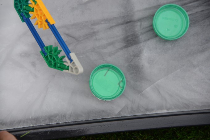 a sheet of ice, a toy hockey puck and two milk bottle top lids for an ice hockey science investigation