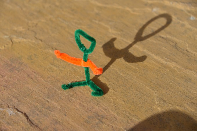 shadow figure made with two pipe cleaners. The figure is stood up outside on a patio and the shadow is clearly visible