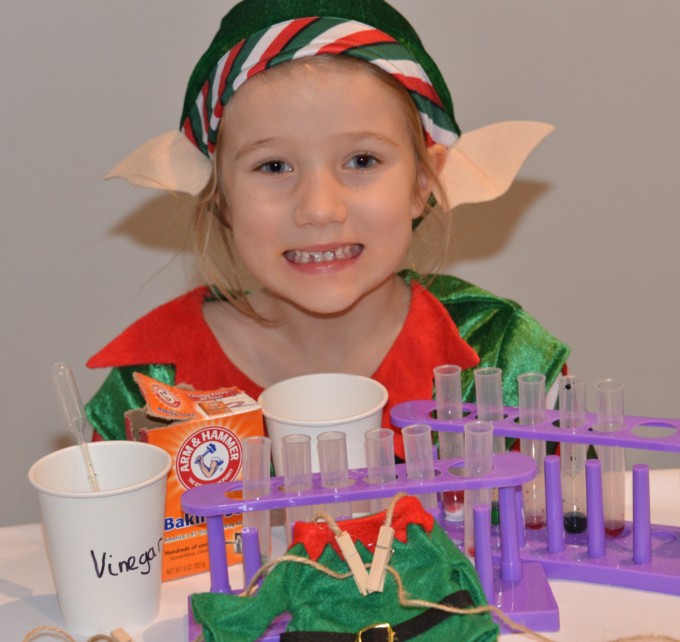 Fizzy Elf Lab - child sat behind test tubes and a container of baking soda and vinegar