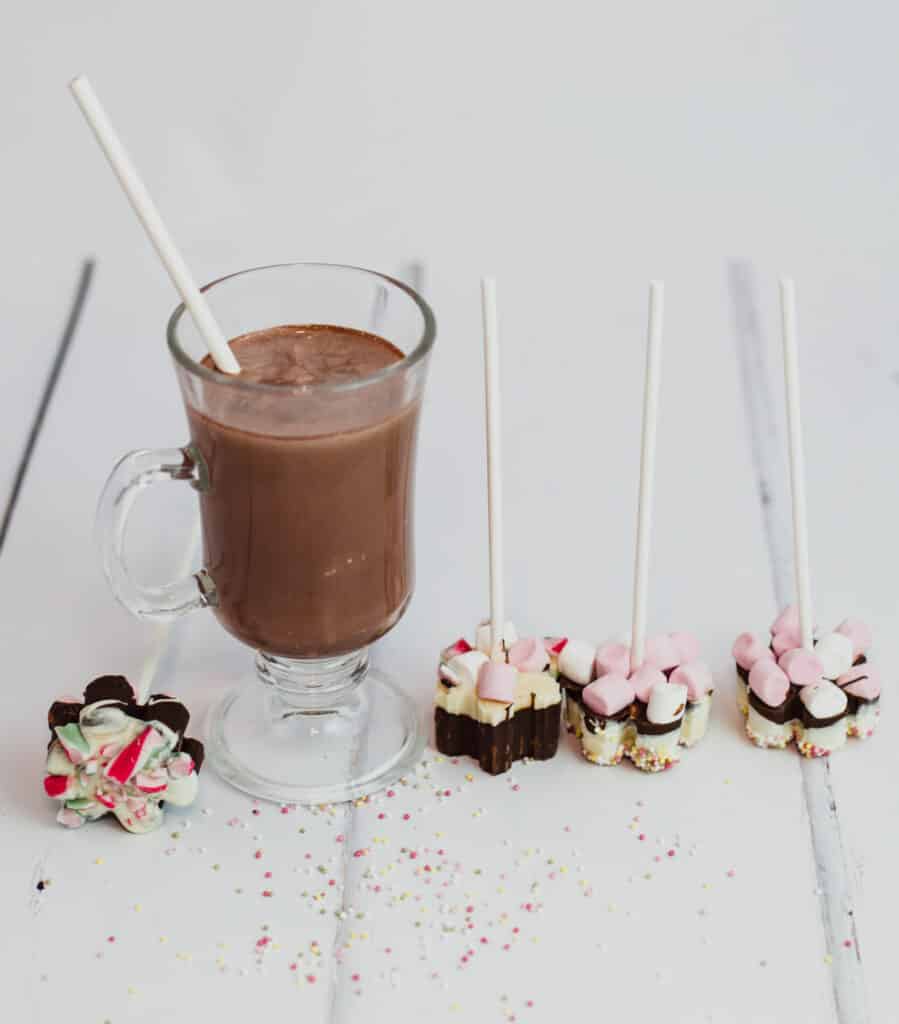 Hot chocolate in a glass and 4 homemade hot chocolate sticks with marshmallows on top