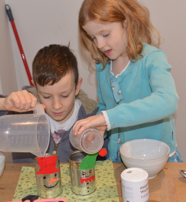 children pouring ice and salt into a tin can to make frost appear on the outside.