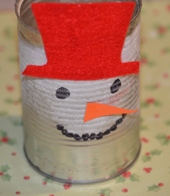 A tin can decorated like a snowman using a black sharpie and orange paper for a nose. Frost has formed on the outside of the can which il full of water, ice and salt.