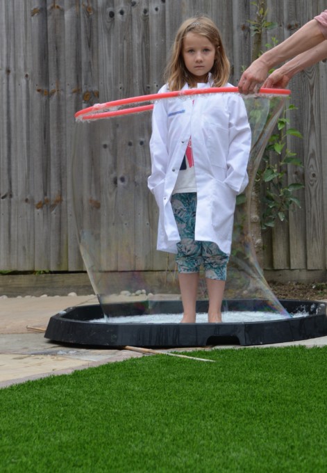 child inside a giant bubble made using a tray and a hula hoop