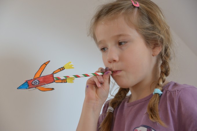 Child blowing down a straw to make paper rocket fly